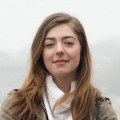 Woman with a subtle smile standing against a plain background.